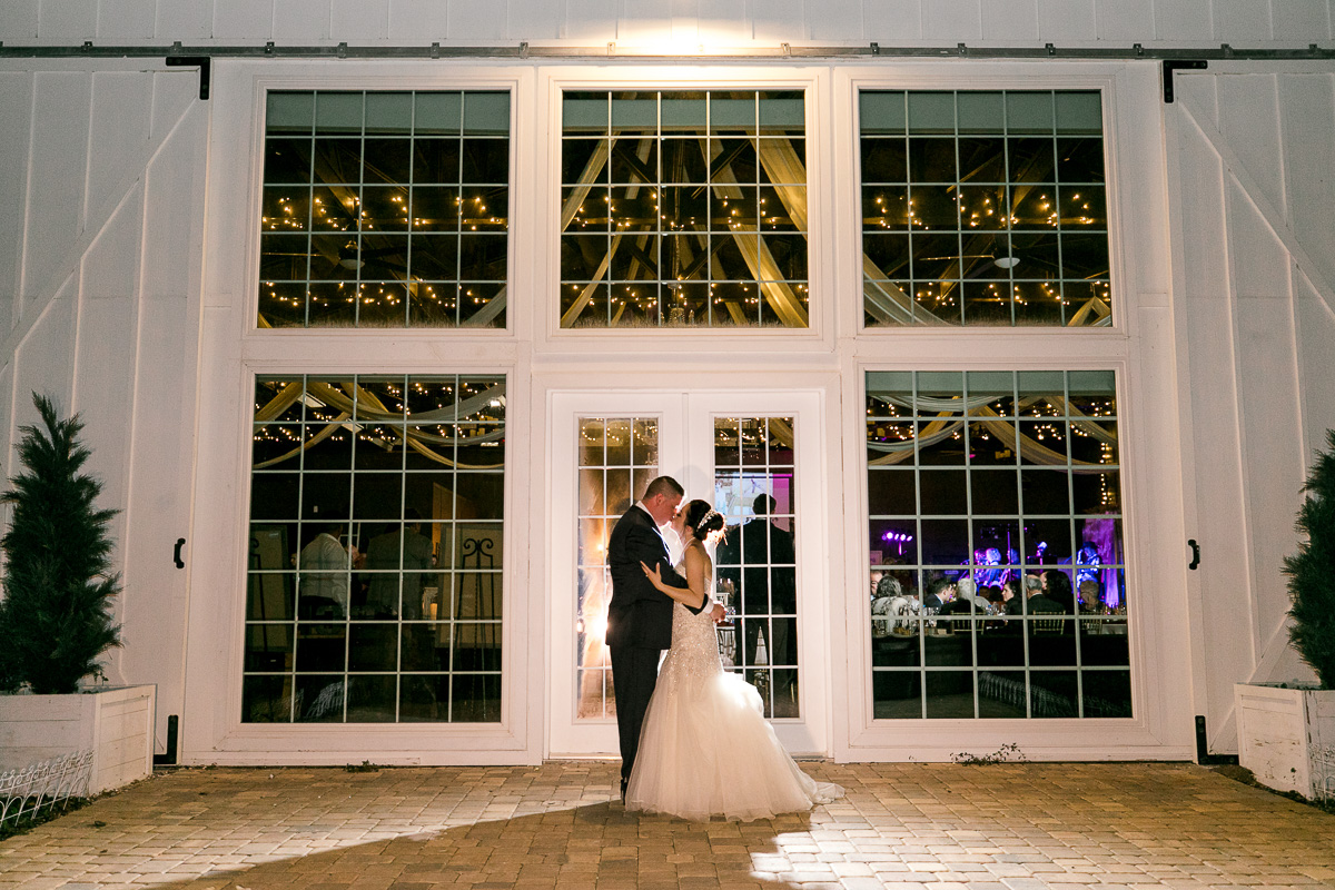 Bride and groom kiss outside in the moonlight in front of white barn