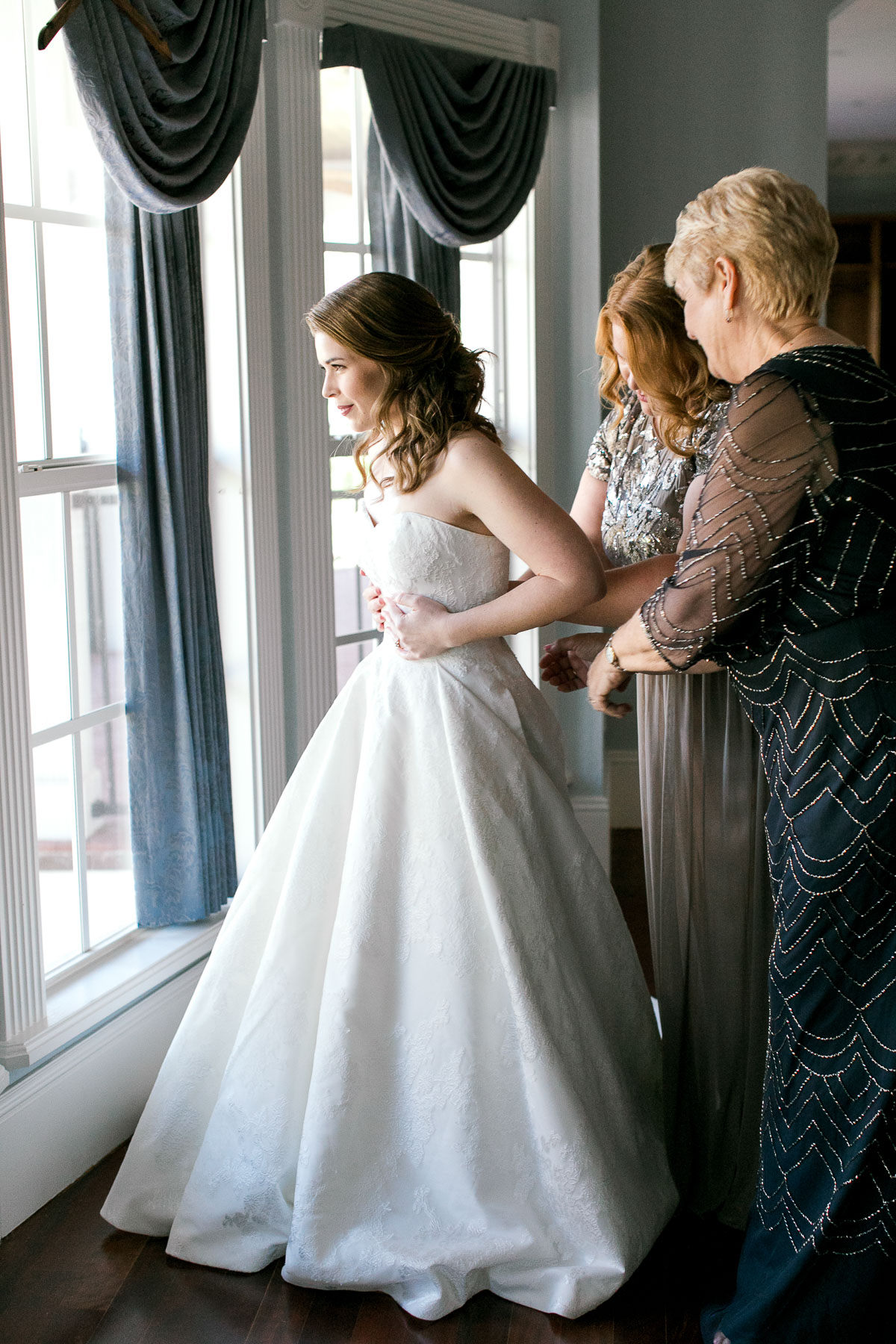Bride's wedding party helping her into wedding dress by Justin Alexander