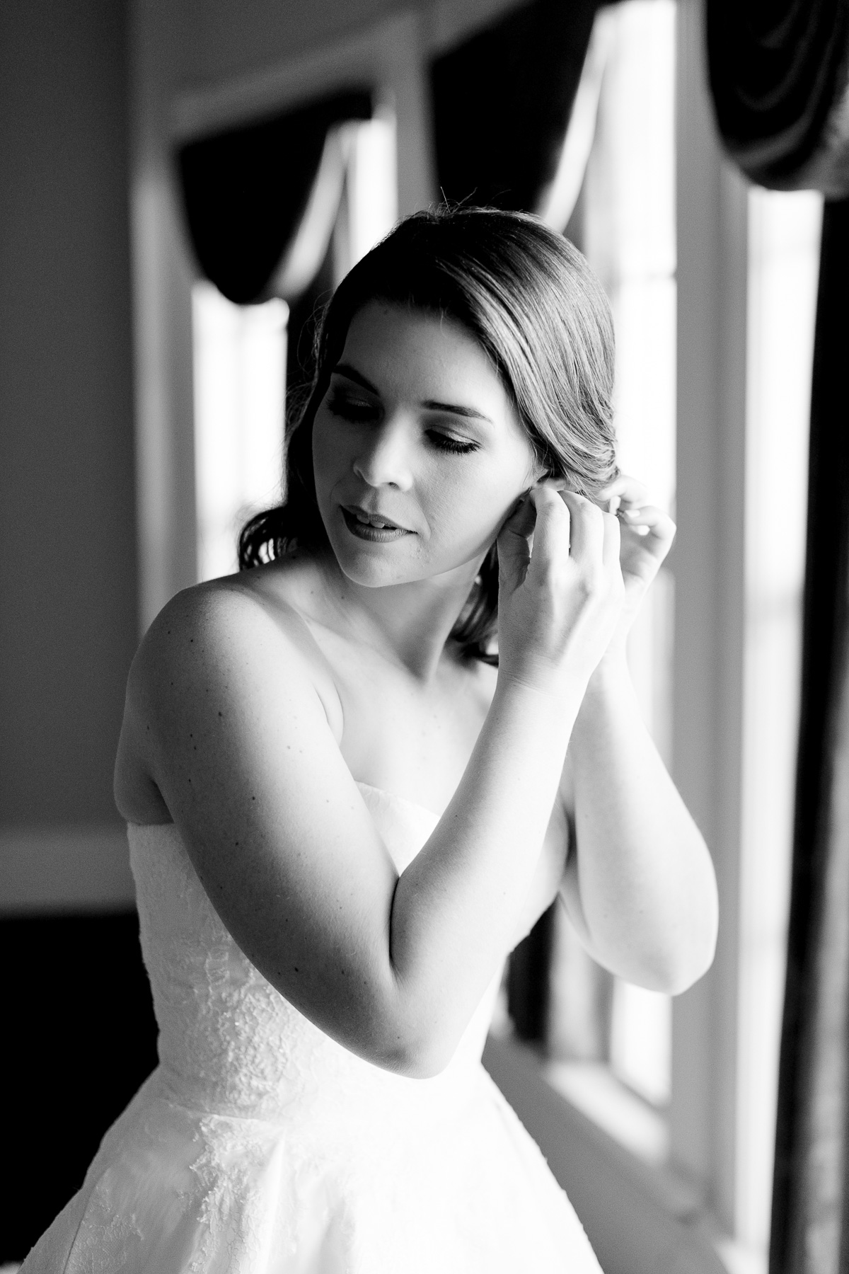 Black and white photo of bride putting on her earrings