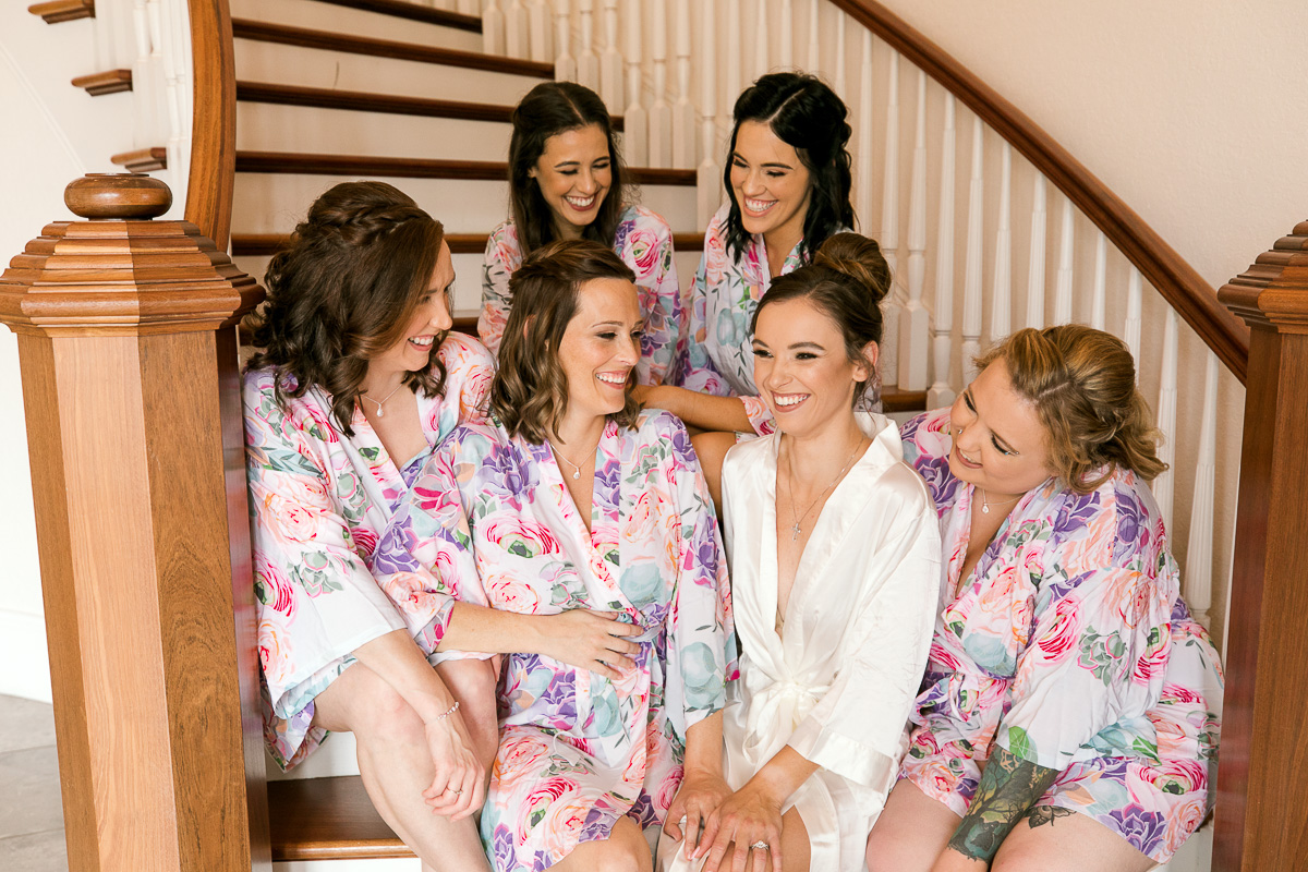Bride laughing with her bridesmaids while sitting on the stairs of Luxmore Grande foyer. 