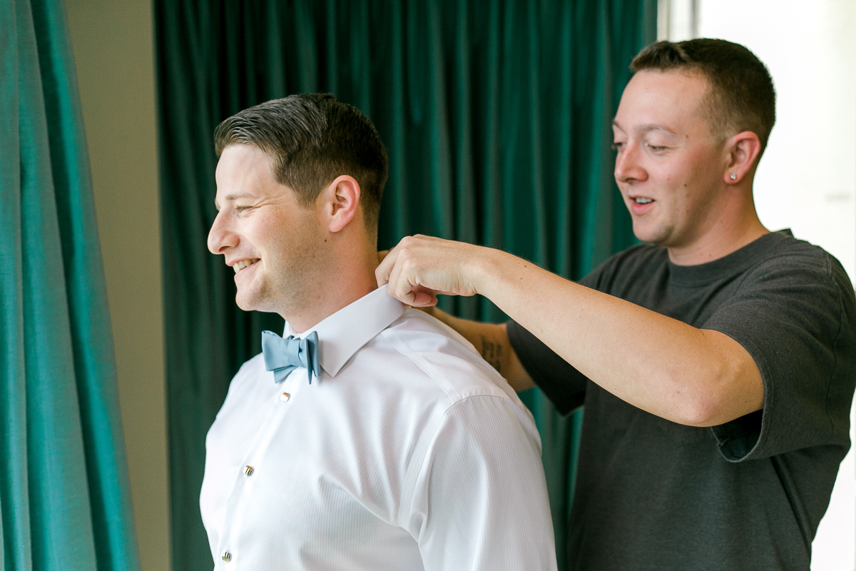 Groomsman helping groom fix his collar 