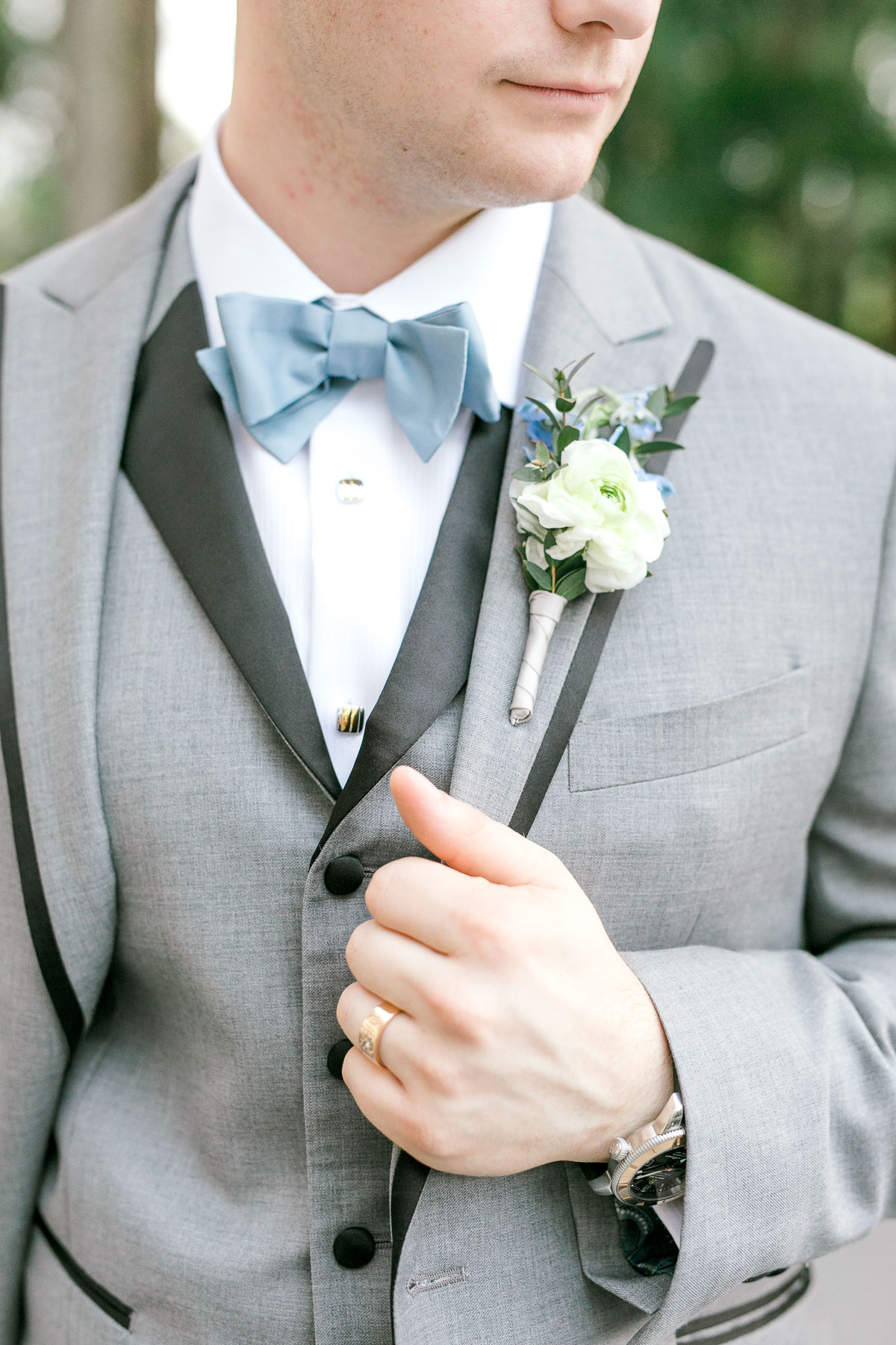 close up of grooms gray tux and blue bowtie, white and blue boutonnière 