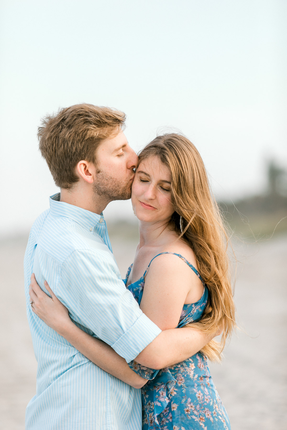 Guy kisses girl on the side of the head at beachside engagement session