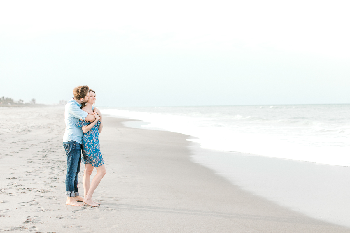 Engaged couple stand along the shoreline looking out into the water