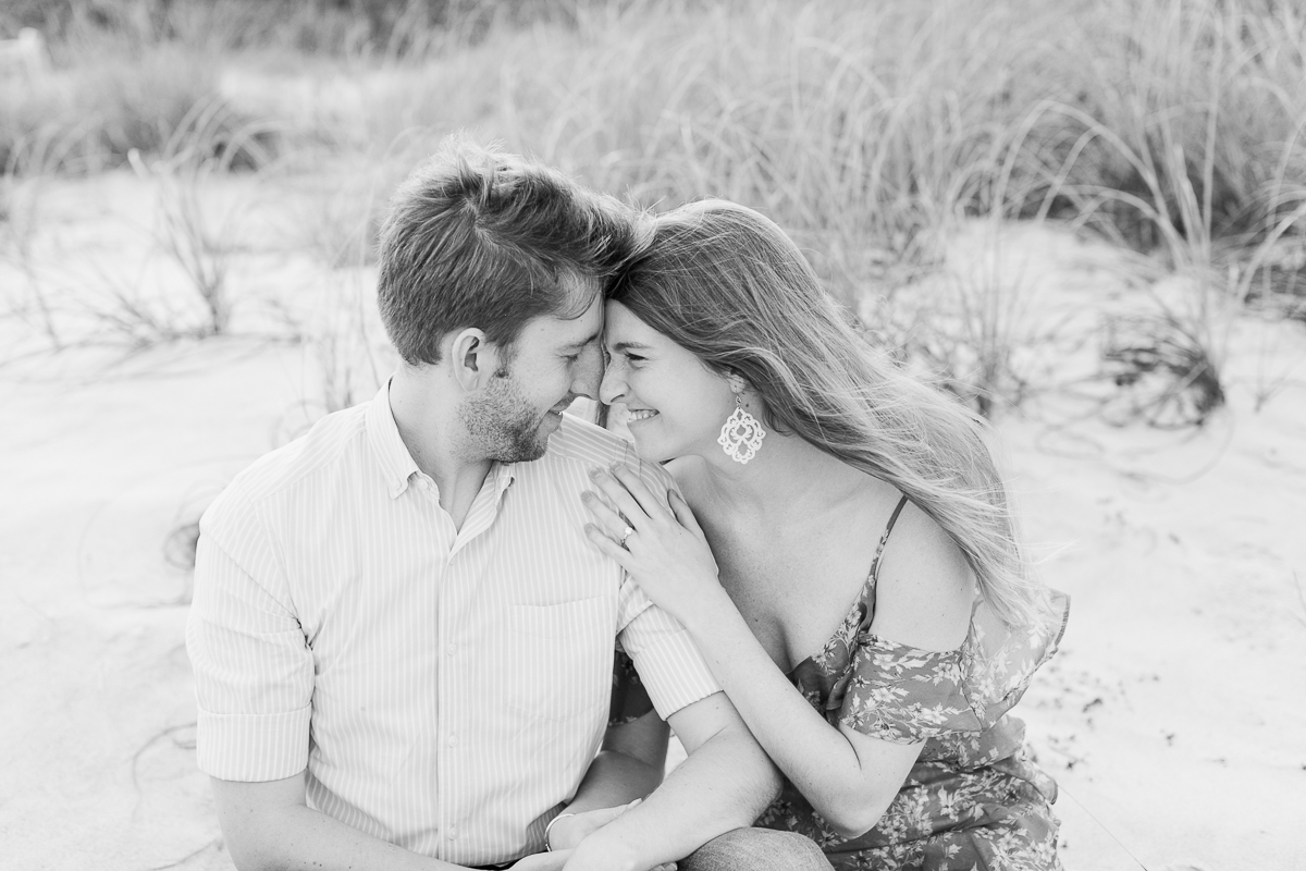 Black and white photo of couple sitting on the sand at their romantic engagement session 