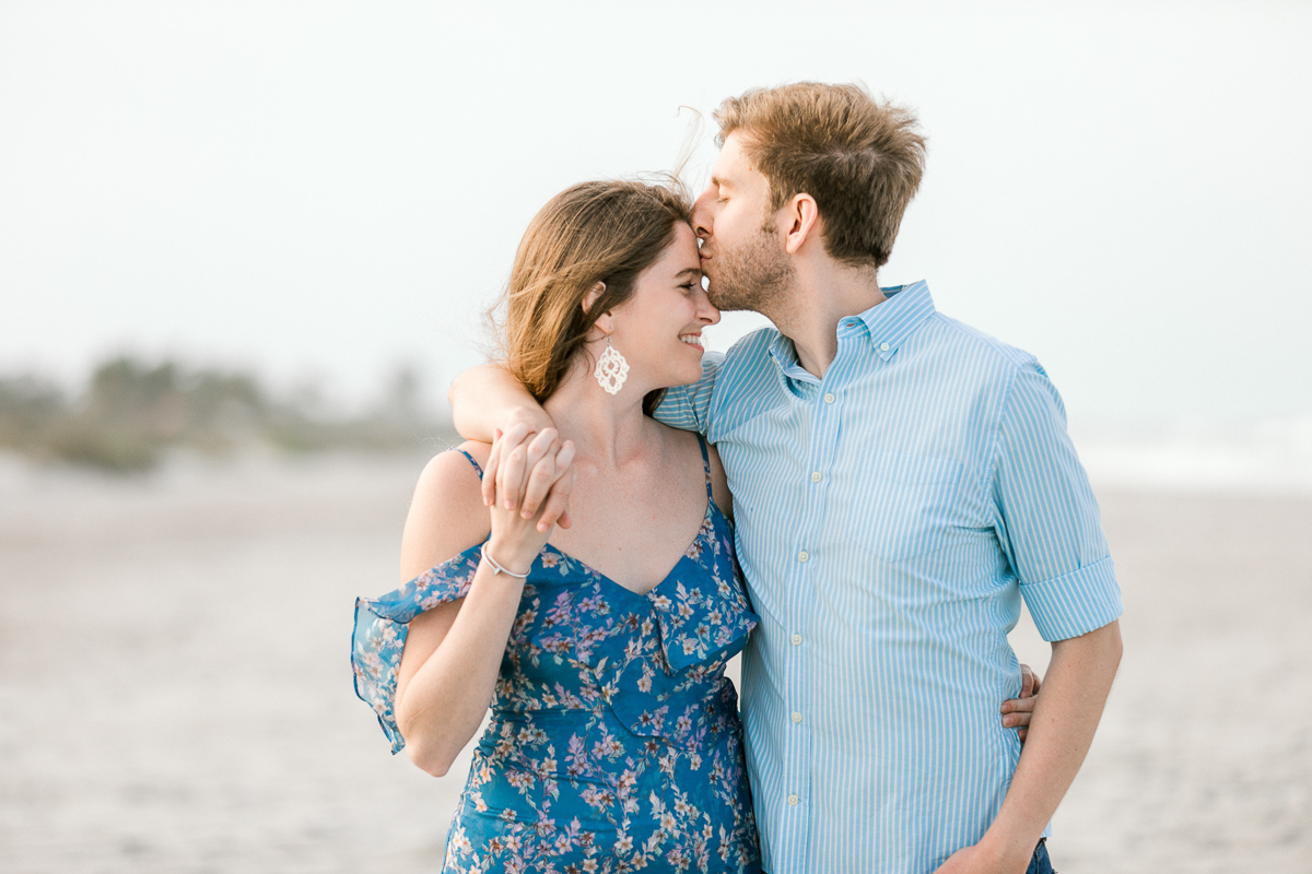 Guy kisses girl on the forehead while standing on the shoreline