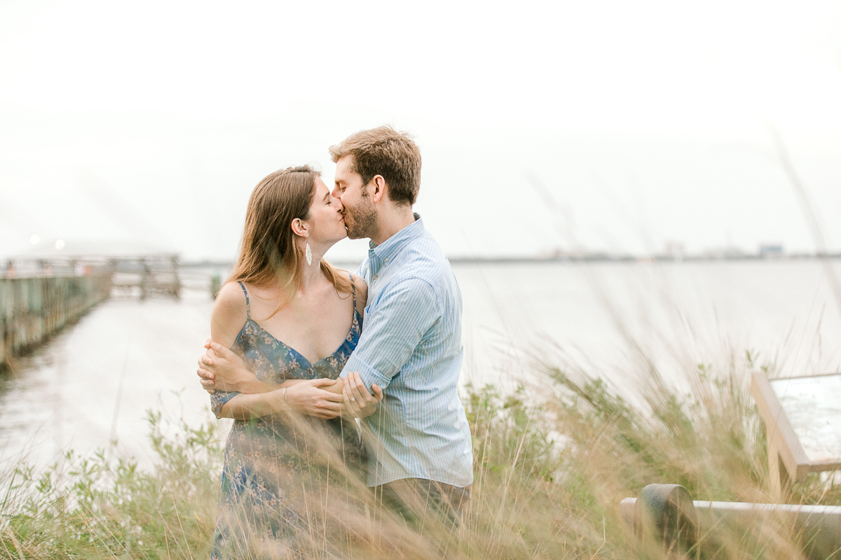 Couple kissing among the shoreline plants at engagement session 
