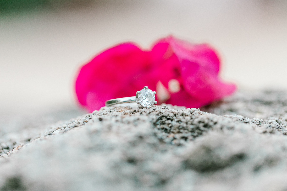 Woman's silver diamond engagement ring with bougainvillea flowers in the background. 